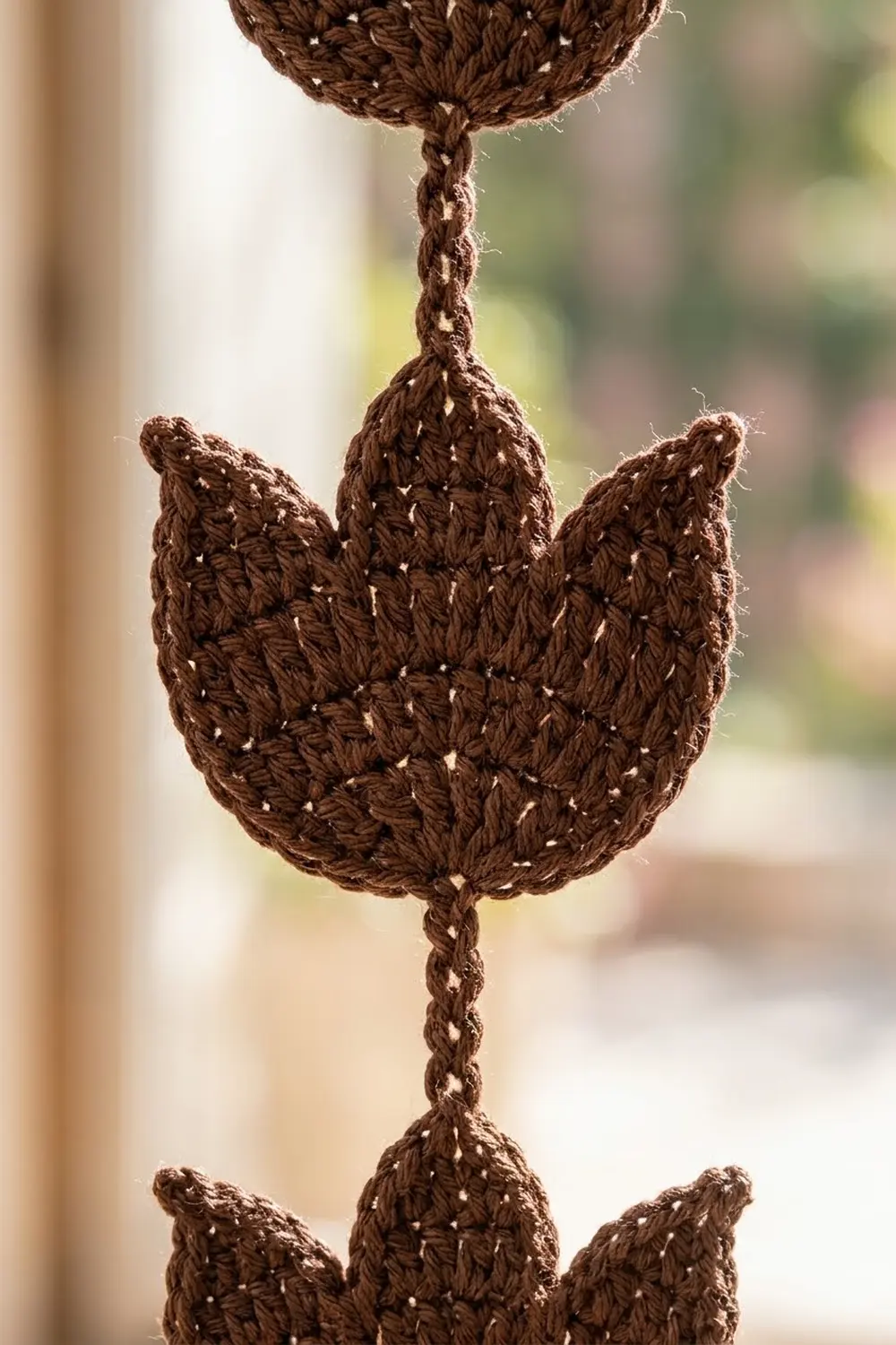 Crocheted brown cactus with white beaded details hung against a softly blurred natural light background.