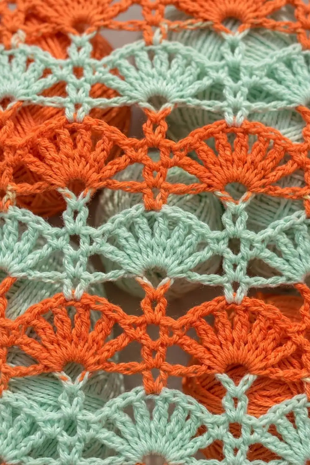 Detailed crochet lace in alternating orange and mint green rows with scalloped openwork pattern on gray background.