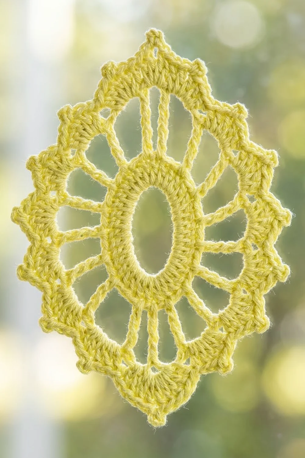 Bright yellow handmade crochet lace ornament with intricate openwork displayed against soft-focused green nature background.