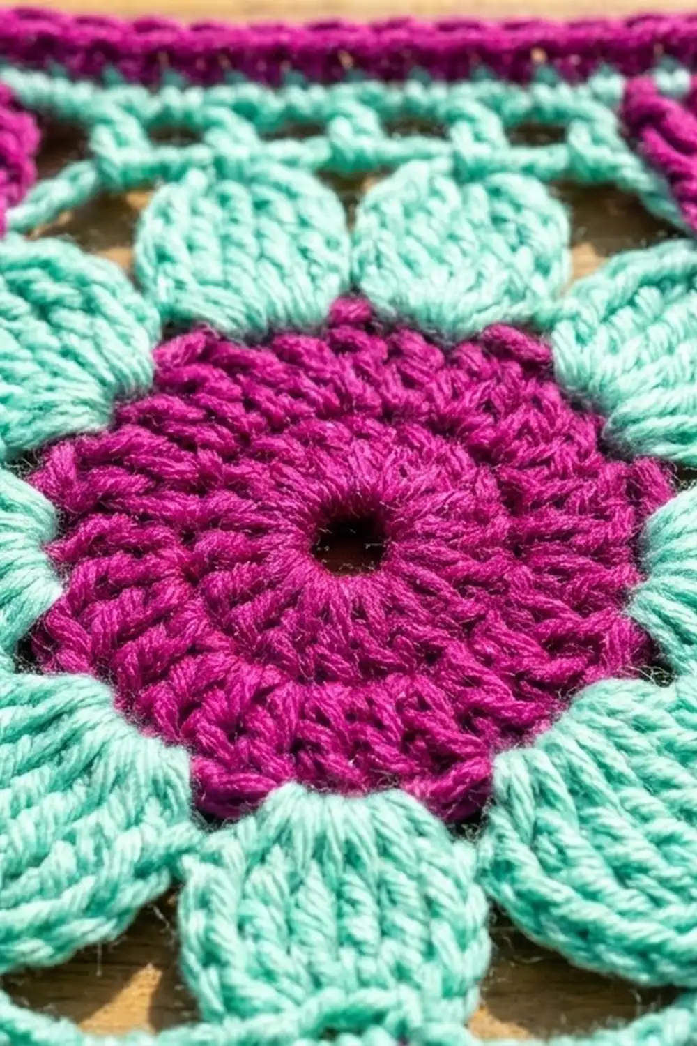Close-up of crocheted magenta flower with mint-green petals showing detailed yarn texture and stitching.