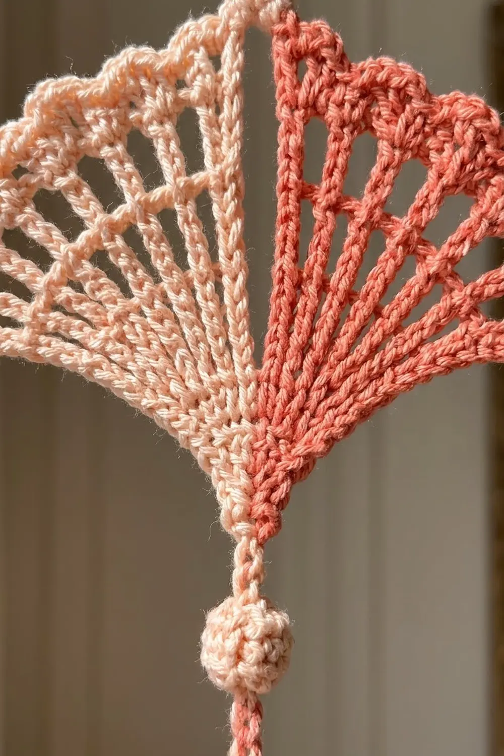 Two-tone crocheted heart in cream and coral colors with detailed stitch work photographed against a neutral background.