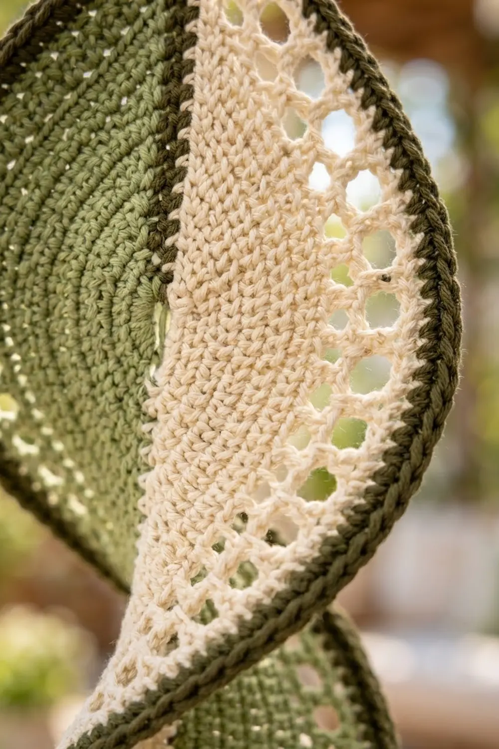 Folded crocheted fabric showing olive-green textured section next to cream lace edging with eyelet holes.