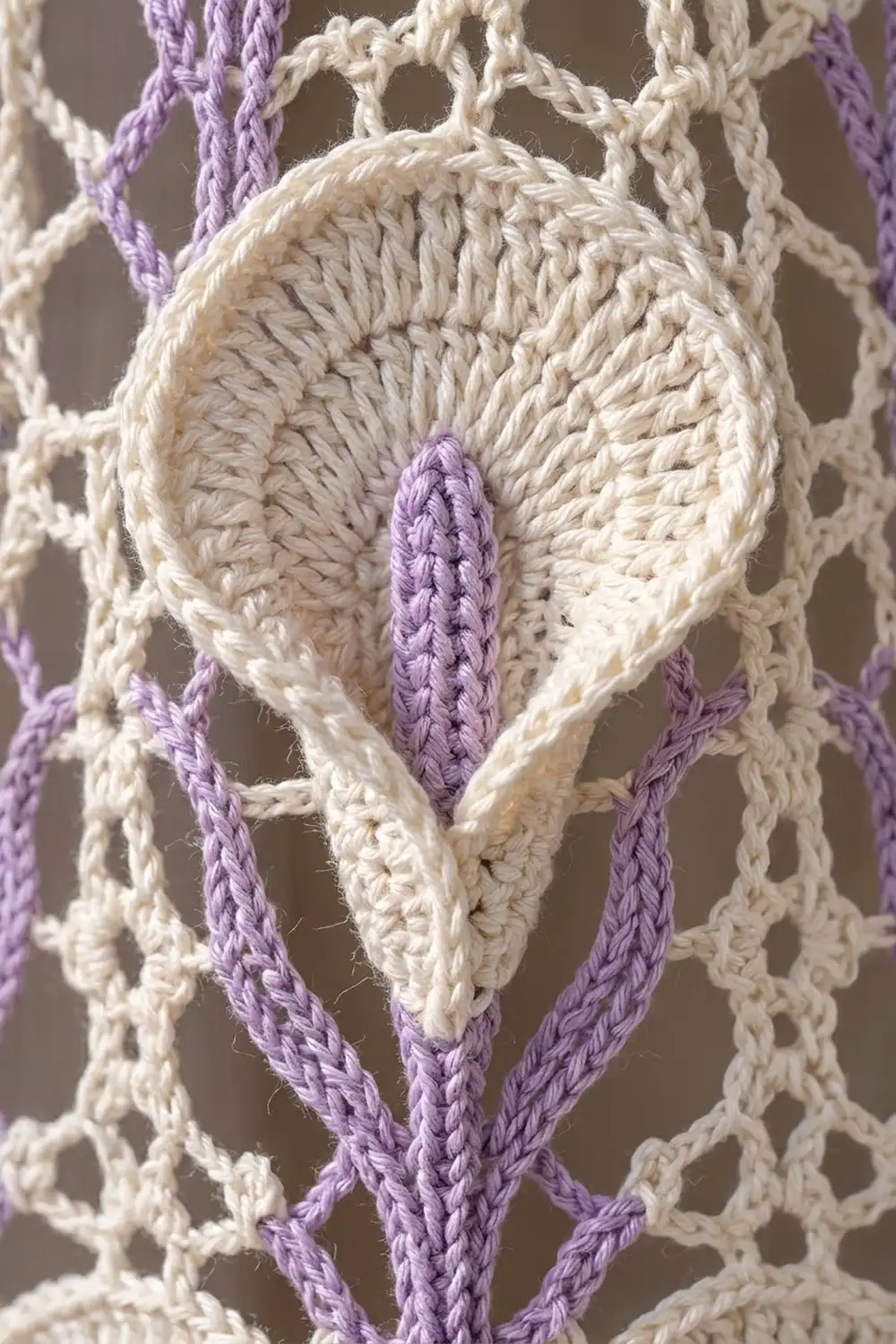 Macramé wall hanging detail showing cream and purple braided cords in a diamond knot pattern.