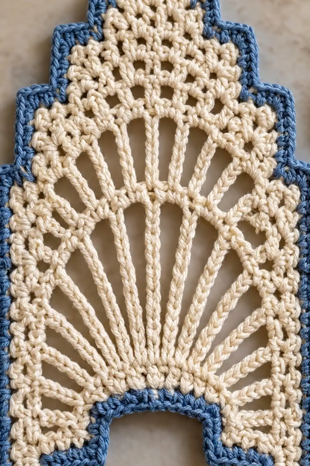 Cream-colored crochet with blue borders showing an intricate openwork fan-stitch pattern against a neutral, light background.