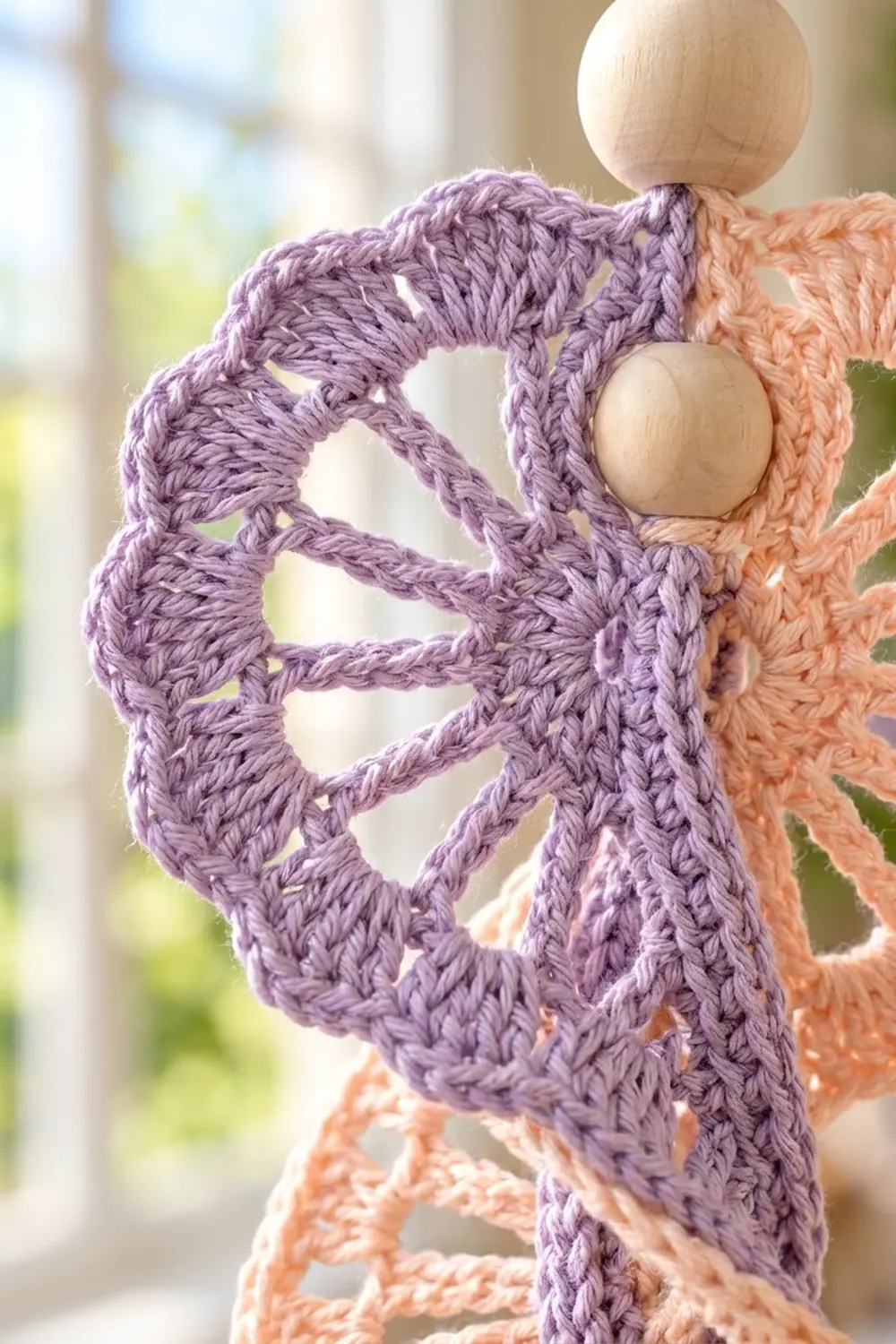 Crocheted lace in purple and peach yarn with wooden beads set in open stitches, backlit.