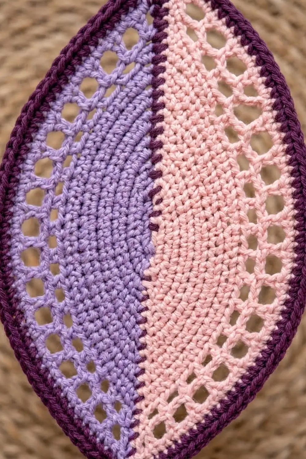 Close-up of triangular crocheted piece with openwork pattern in deep purple, lavender, and pale pink stripes on beige background.