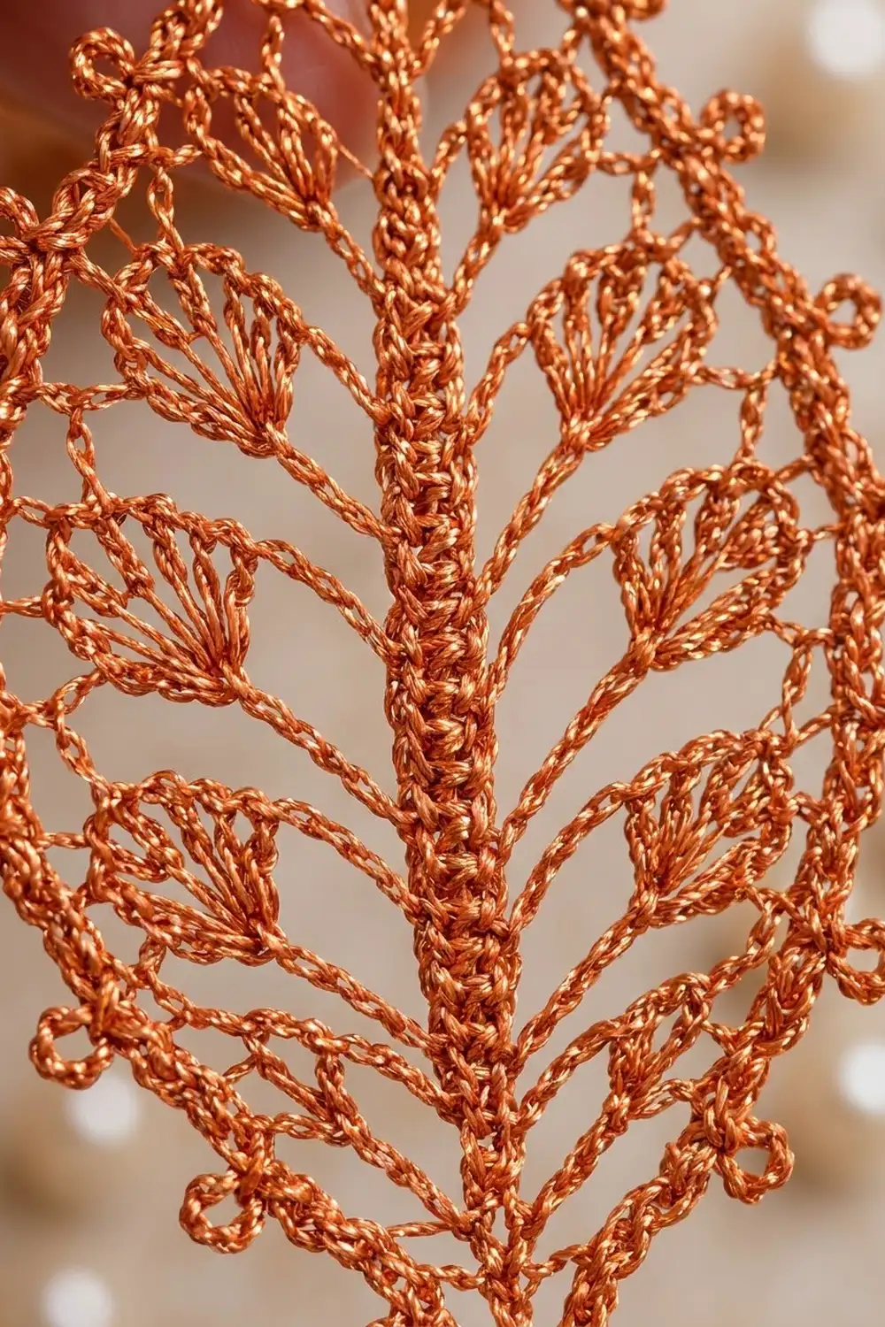 Crocheted copper yarn branching into delicate, symmetrical fern-like patterns against a soft beige background.