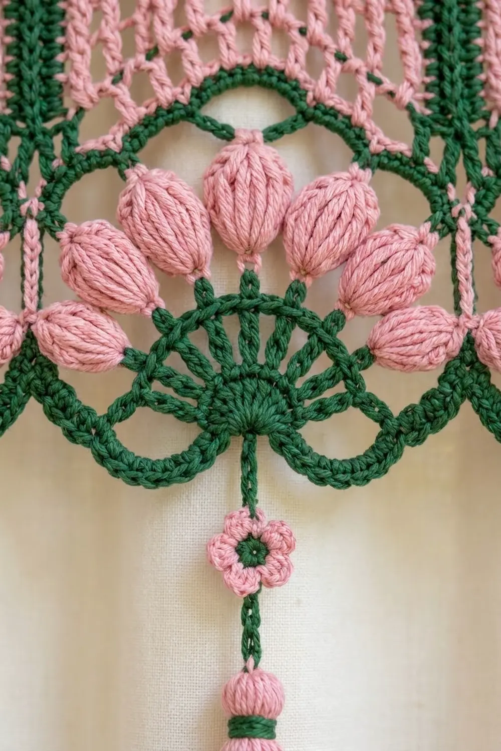 Crocheted pink flowers with textured petals connected by delicate green lace framework on cream fabric.