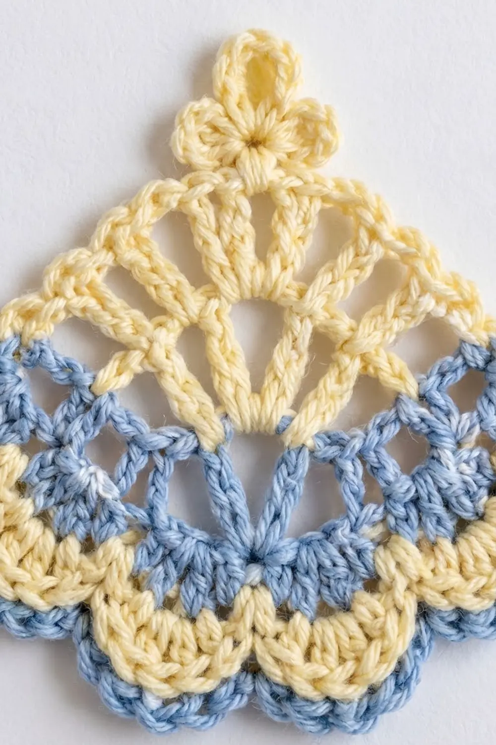 Crocheted figure in cream yarn with outstretched arms and blue shell-stitch trim on white background.