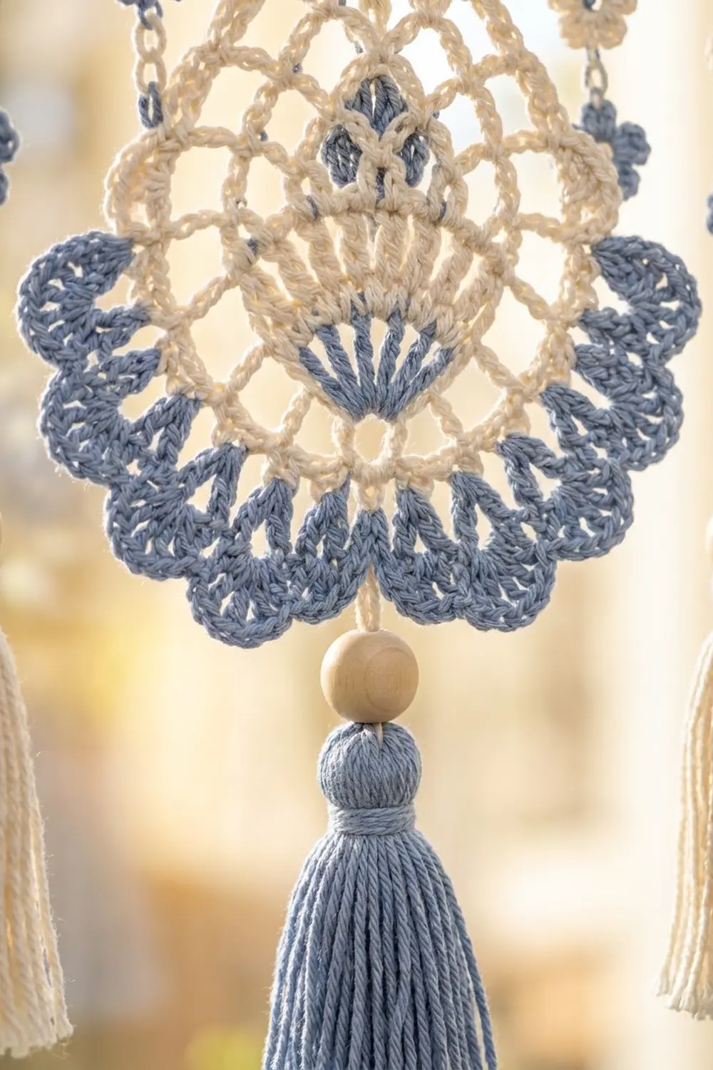 Intricate crocheted ornament in cream and slate blue with wooden bead center and dangling tassel.