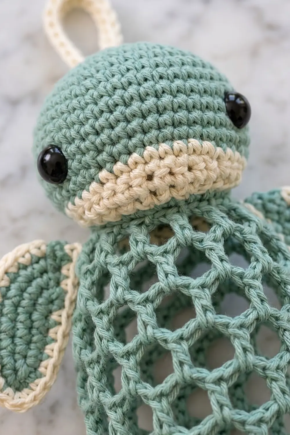 Sage-green crocheted octopus with cream-colored mouth stripe, black bead eyes, and visible stitch detail texture.