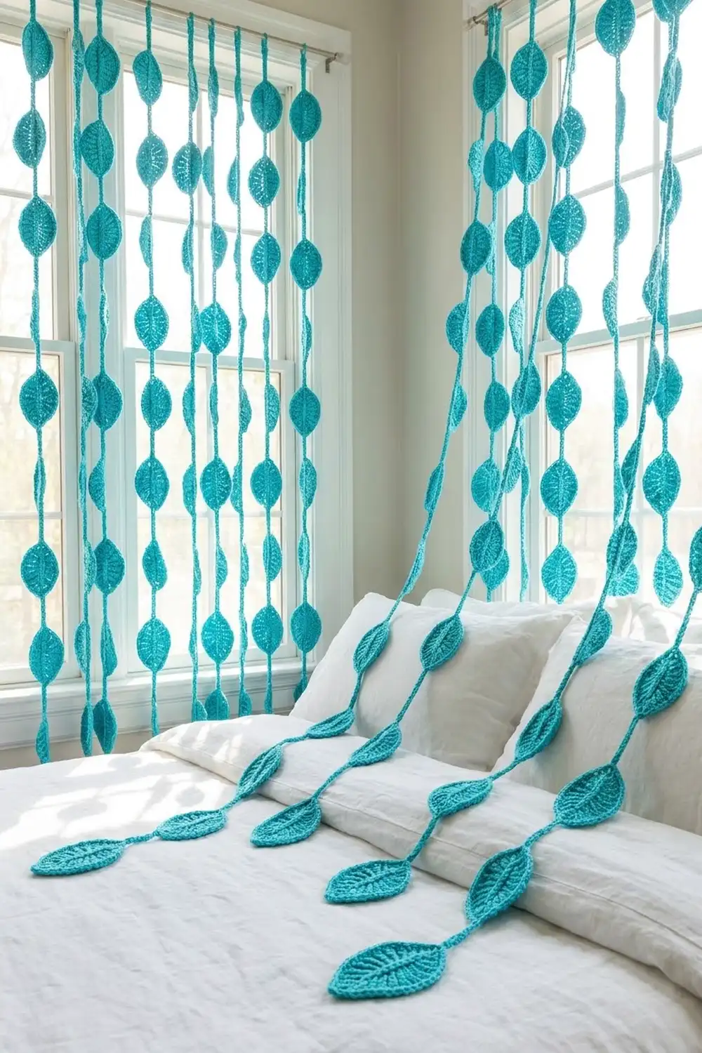 Turquoise crocheted leaf garland hangs by bright windows, with strands draped across white pillows and bedding.