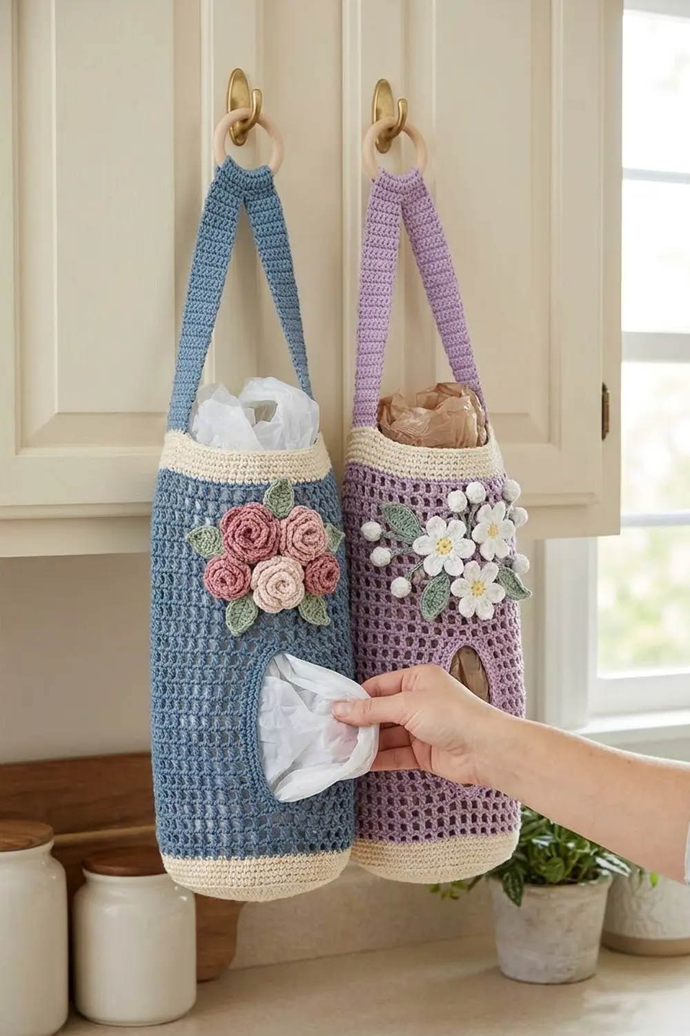 Hand pulling tissue from blue crocheted caddy with pink flowers; matching purple holder decorated with white flowers and wooden rings.