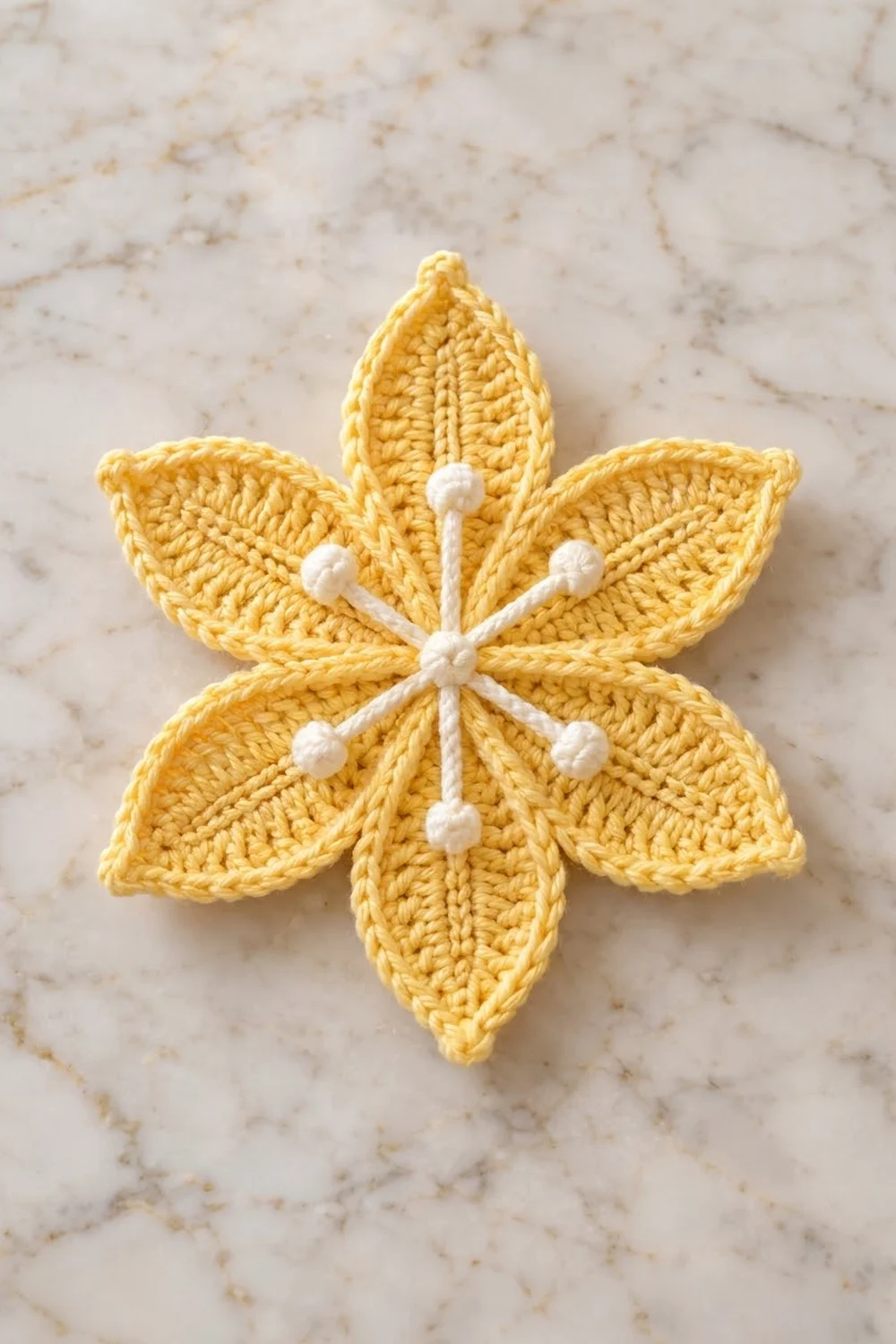 A bright yellow crocheted flower with white beaded center displayed on a marble surface.
