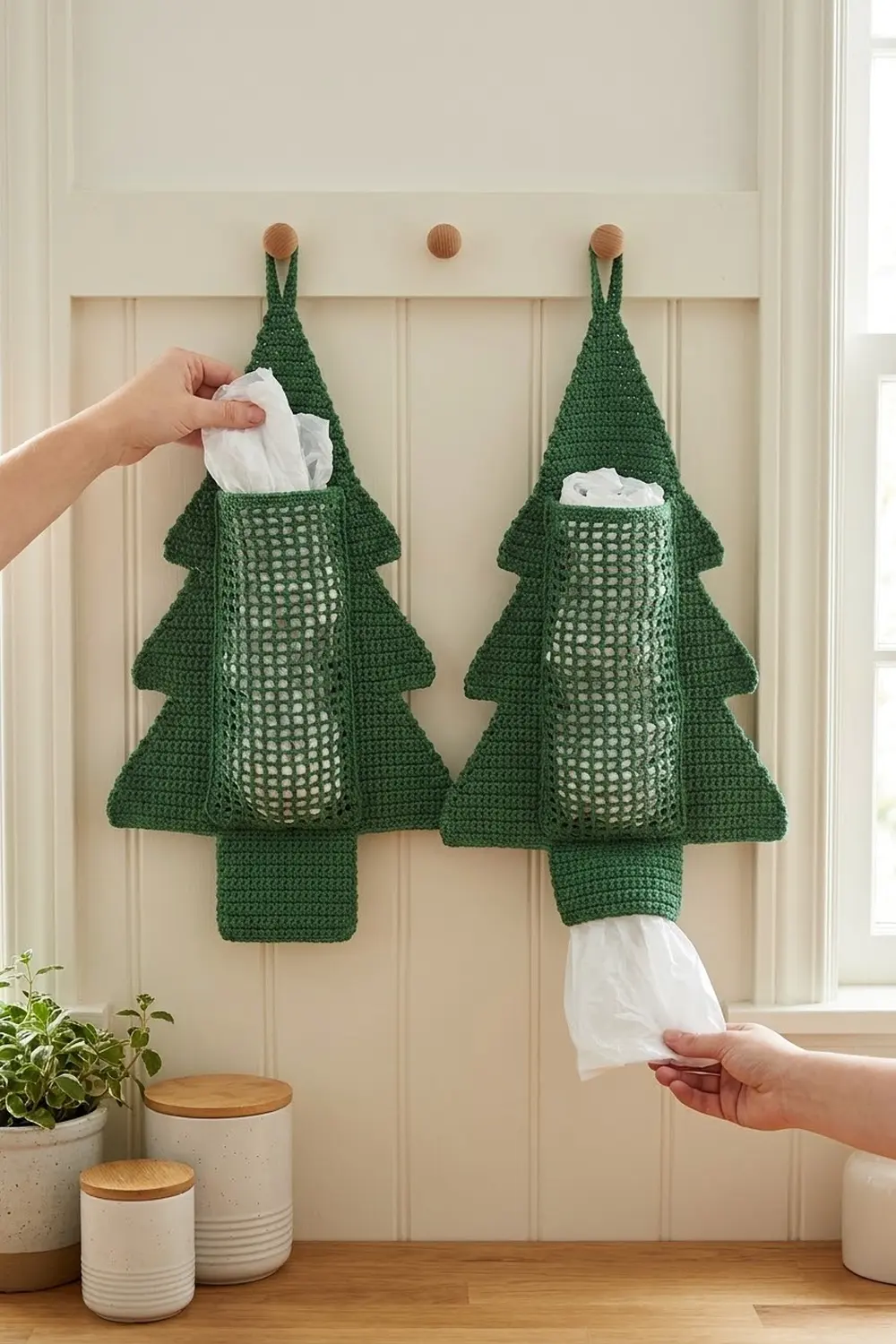 Two dark green crocheted Christmas tree tissue box holders with wooden beads dispensing white tissues on a cream-paneled wall.