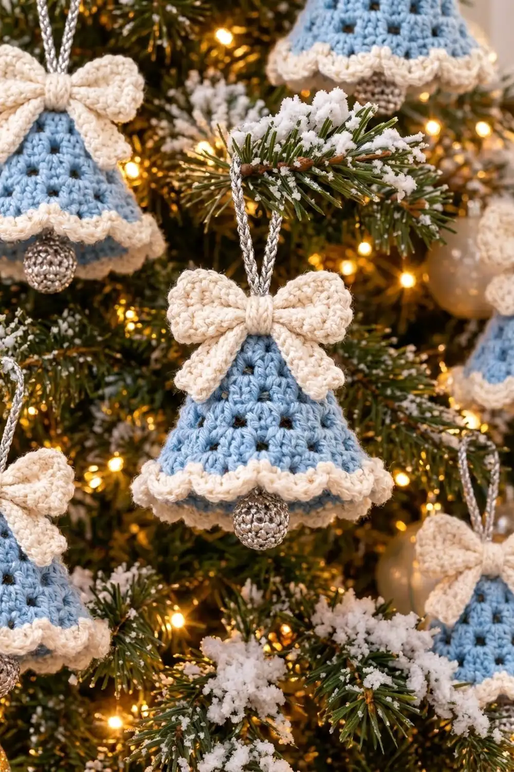Multiple blue crocheted bell ornaments with cream bows and ruffles decorate a lit Christmas tree with frosted branches.