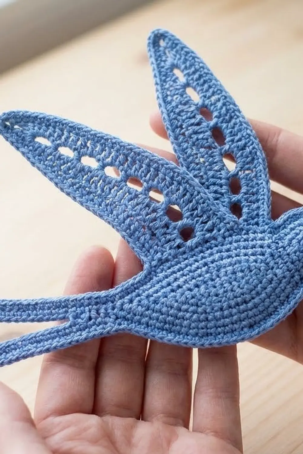 Blue crocheted starfish with openwork holes held in hands against a warm, neutral background in daylight.