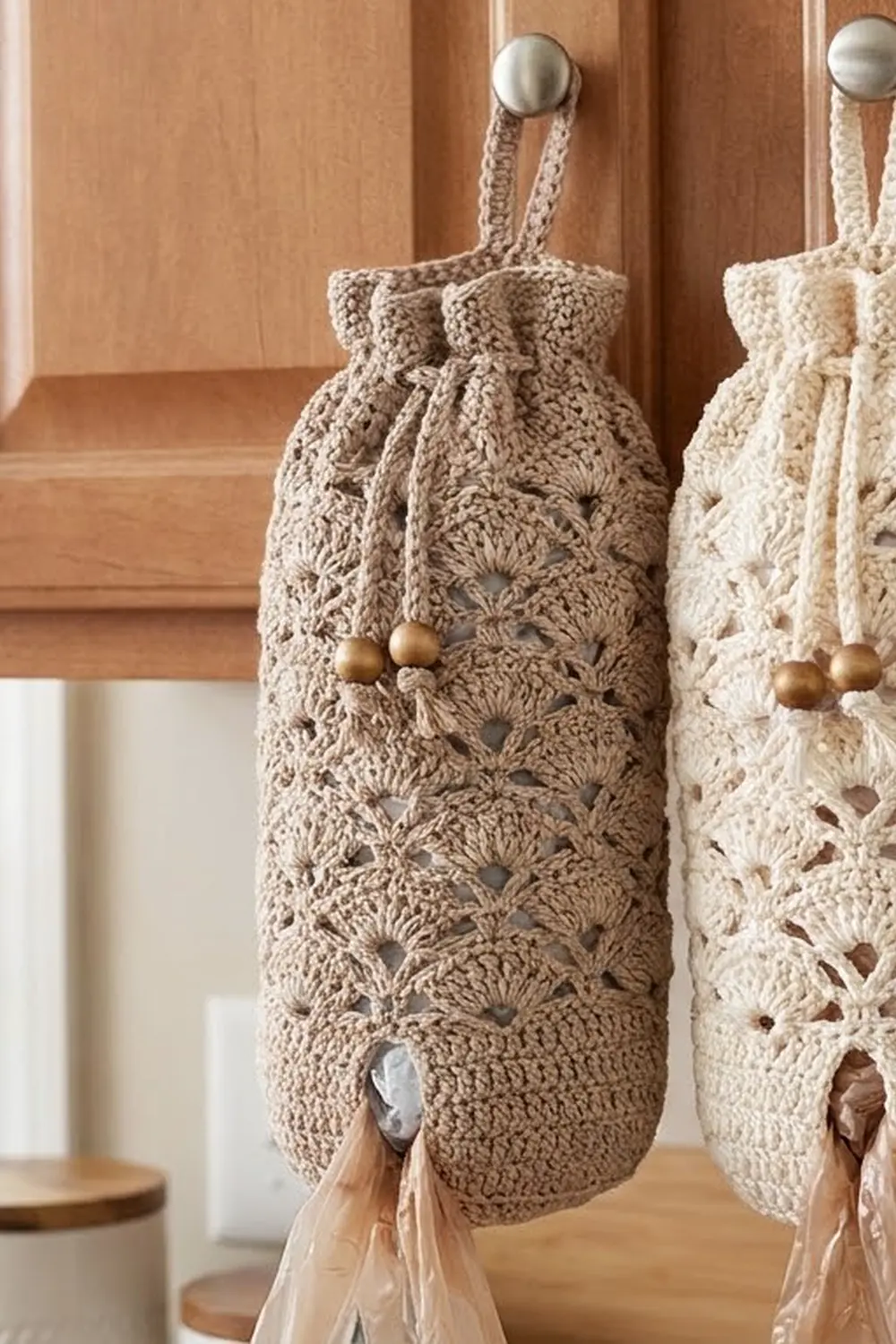 Crocheted drawstring bags in cream and gray with openwork patterns and wooden bead closures hang from warm wooden cabinet knobs.