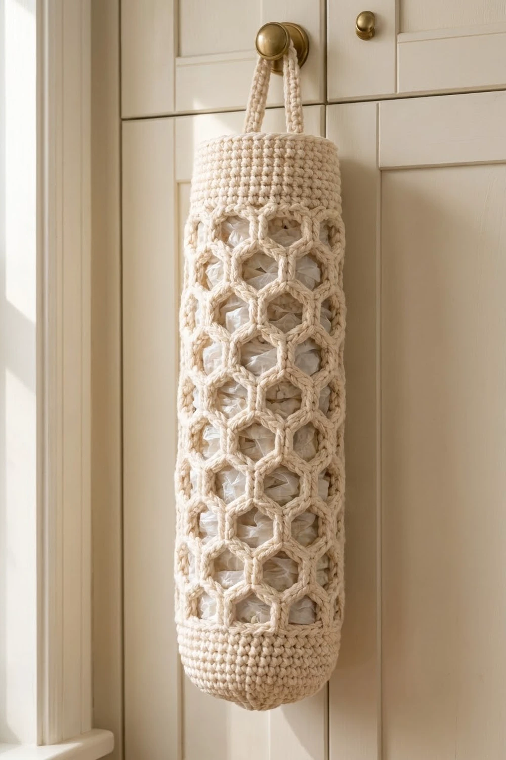Cream crocheted hanging organizer with geometric lattice pattern and rope handles suspended from a brass wall knob.