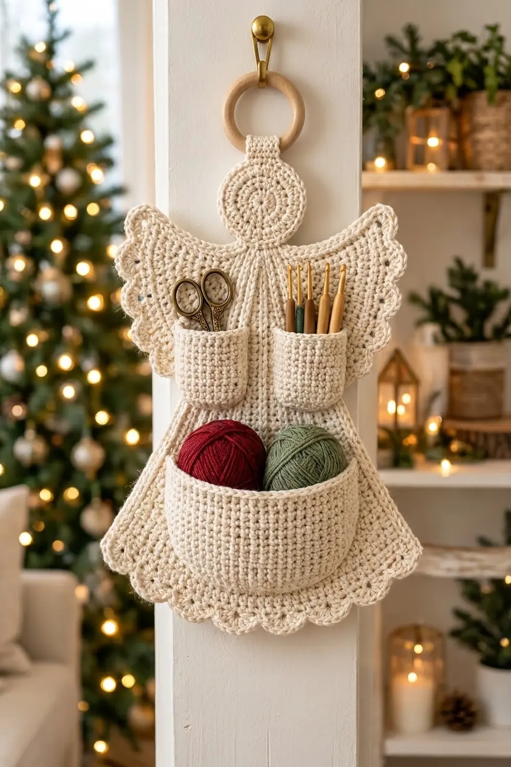 Cream crocheted angel organizer filled with scissors, crochet hooks, red and green yarn on white wall amid festive holiday decorations.