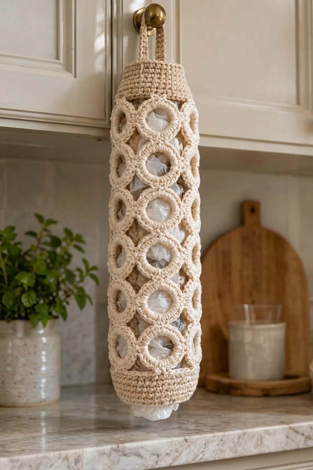 Beige crocheted wall hanging with repeating circular cutouts, hung from a brass hook on neutral kitchen wall.