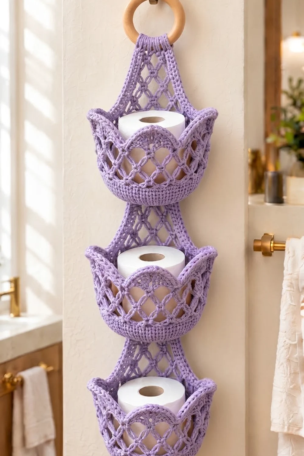 Lavender crocheted toilet paper holder with open lattice pattern holds white rolls on a bathroom wall.