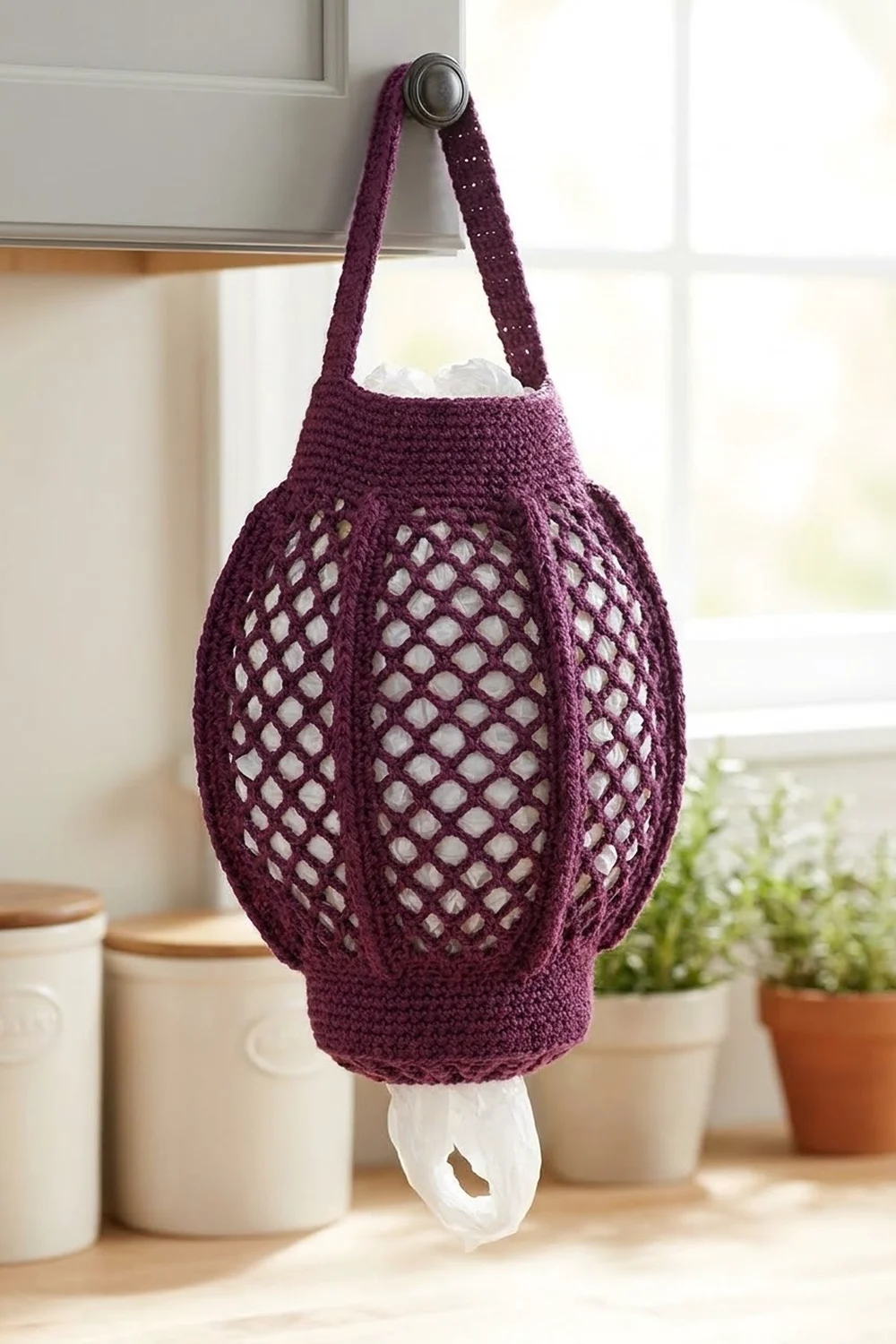 Deep purple crocheted mesh bag hanging on a door hook, holding a white bag inside, with potted plants nearby.