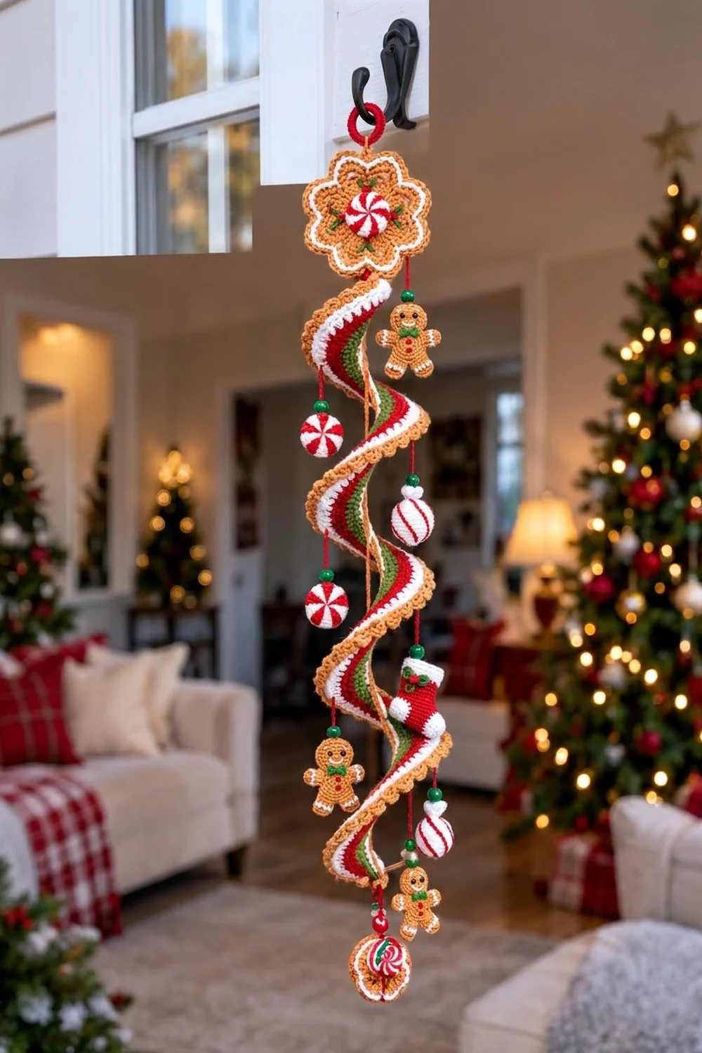 Red, white, and tan crocheted candy garland with gingerbread figures hanging in a festive home surrounded by decorated Christmas trees.