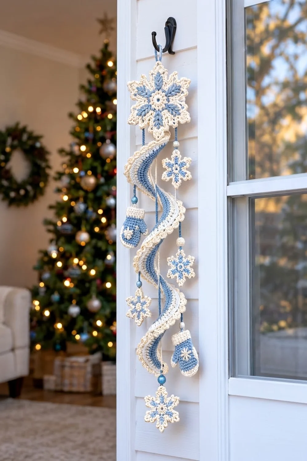 Crocheted blue and cream snowflake mobile displayed on a window with a lit Christmas tree visible in the background.