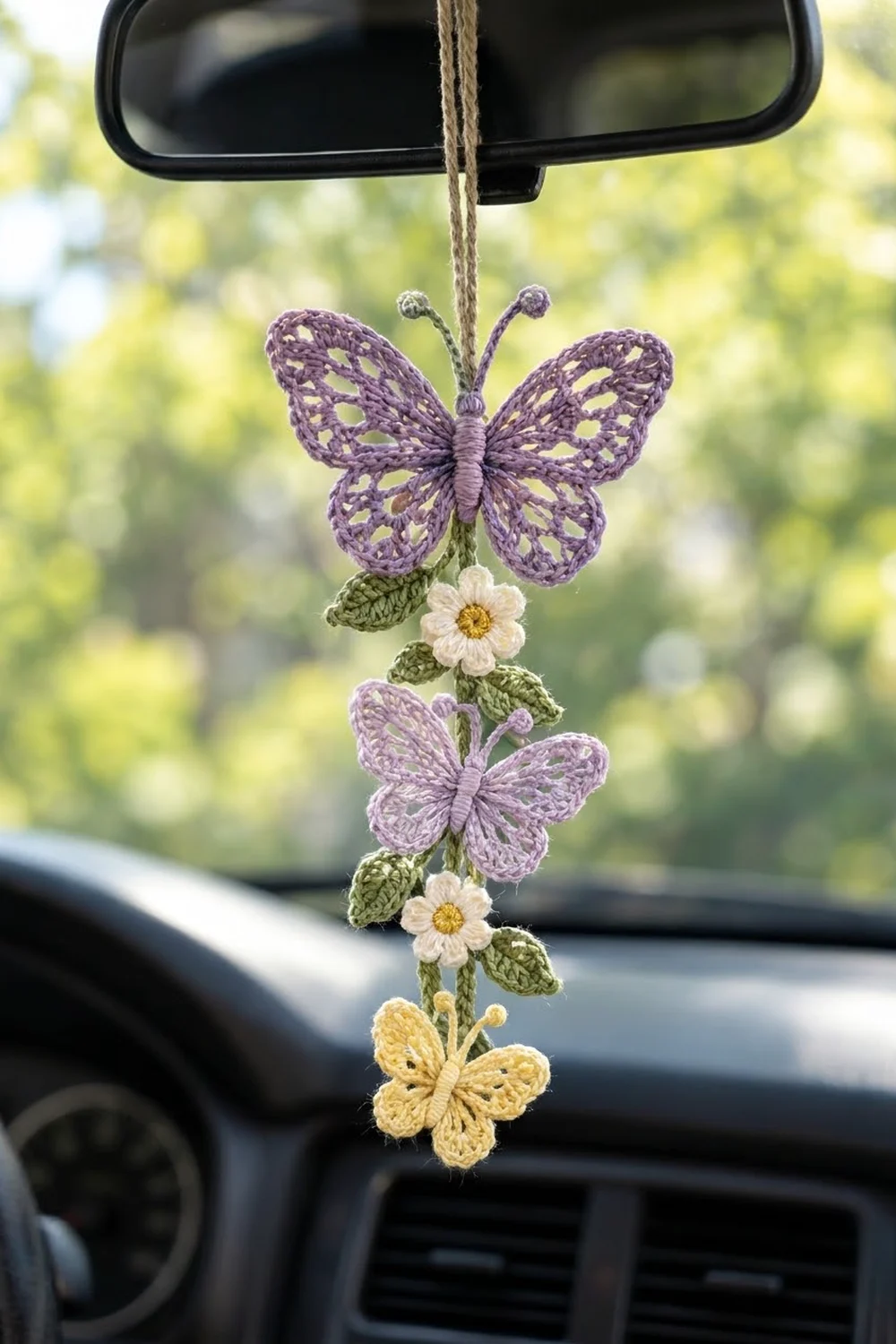 Crocheted purple and yellow butterflies with white daisies hang from a car's rearview mirror against blurred green scenery.