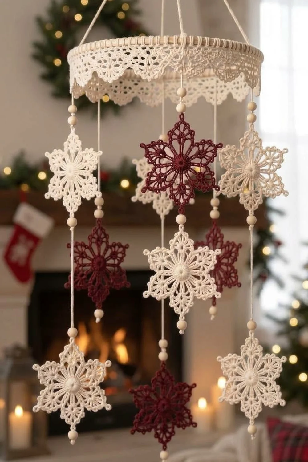 A cream and burgundy lace snowflake mobile hangs in a festive fireplace setting with Christmas decorations.