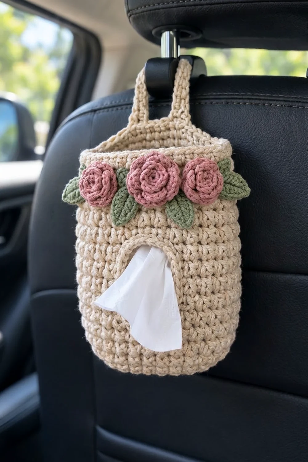 Cream-colored crochet tissue dispenser with three pink roses adorning a car seat headrest.