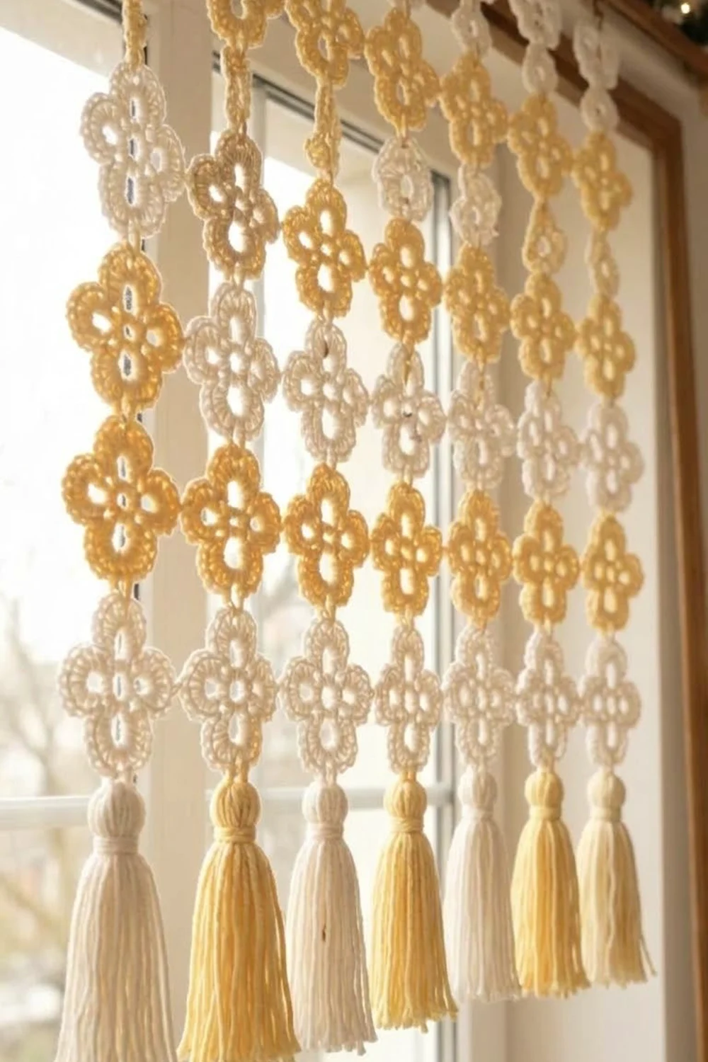 Decorative lace curtain with gold and cream doilies and tassels hanging in a bright window.