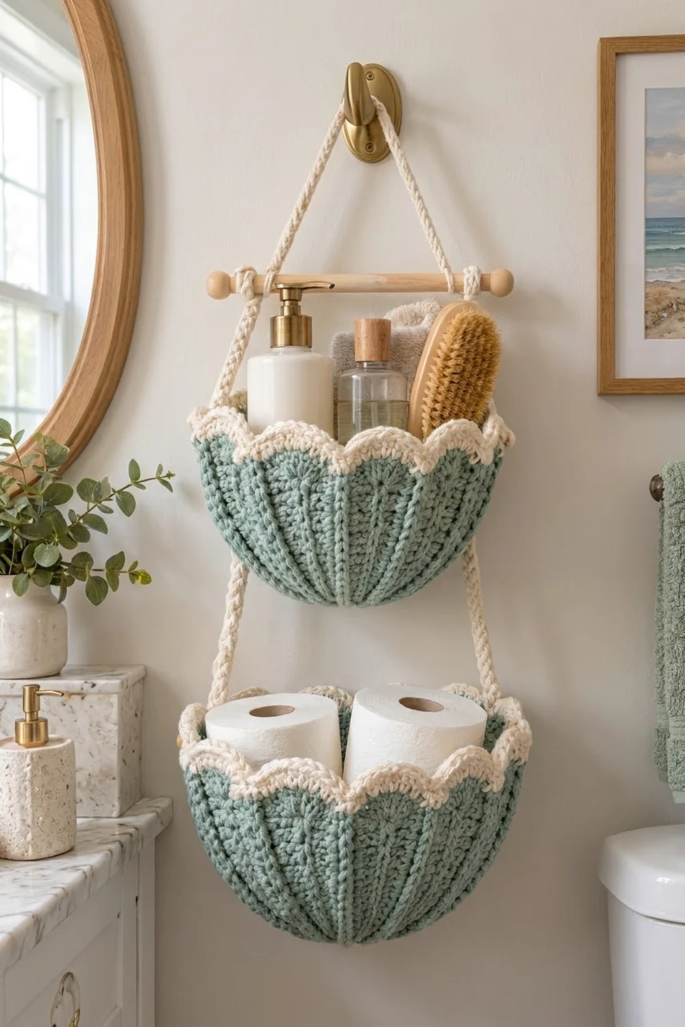 Sage green crochet wall organizer with two hanging pockets holding toilet paper, bottles, and a brush in a bright bathroom.