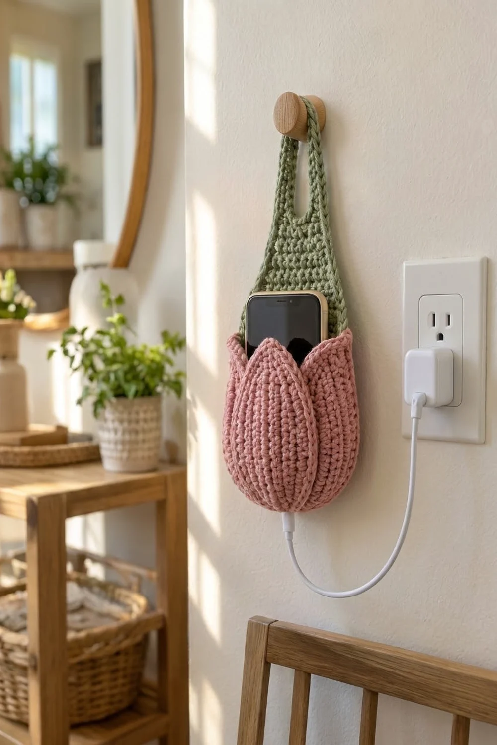 Crocheted phone holder in sage green and dusty rose holding a smartphone on a wall.