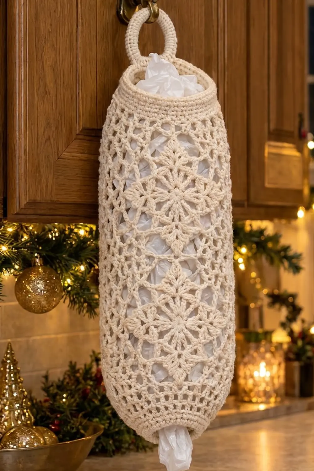 Cream crocheted hanging basket with delicate lace flower pattern displayed amid Christmas ornaments and warm golden lights.