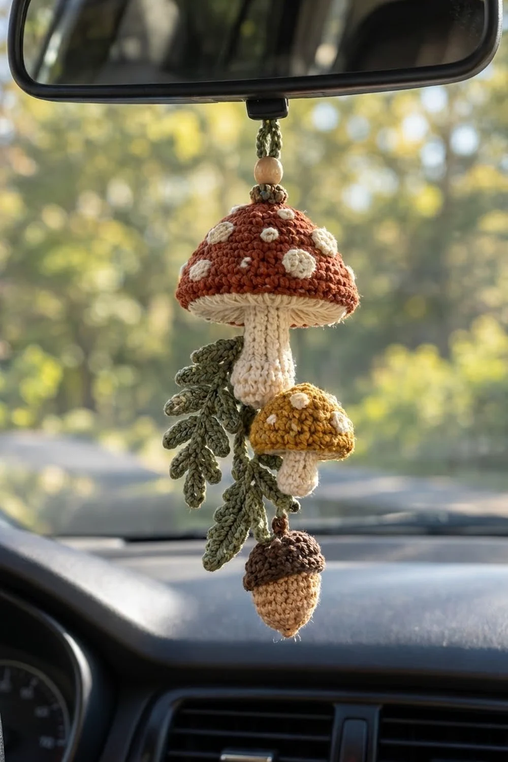 Crocheted woodland charm featuring red toadstool, golden and brown mushrooms, fern leaves hanging from car rearview mirror.