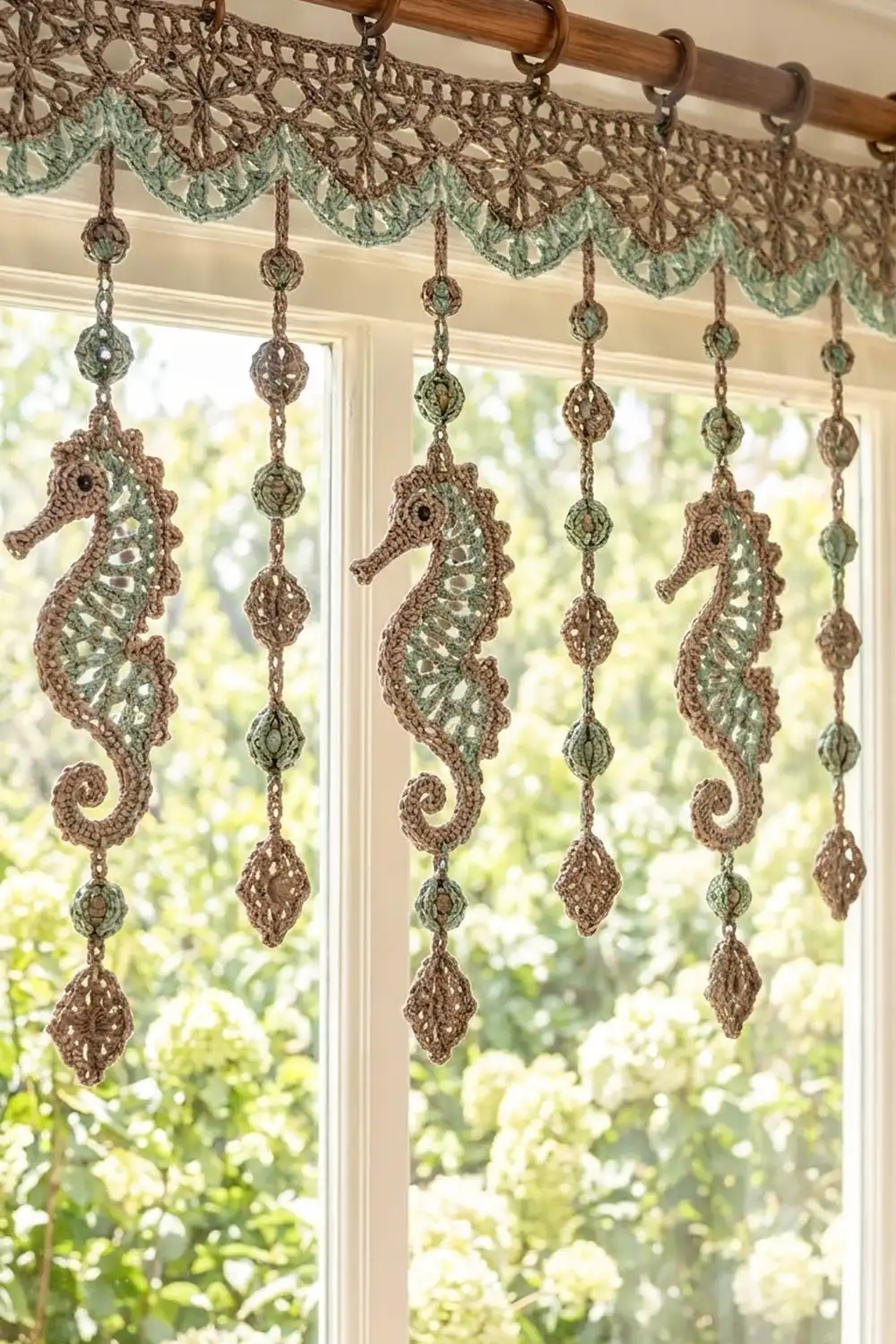 Crocheted window valance in tan and mint-green with seahorse pendants and decorative beads at a garden window.