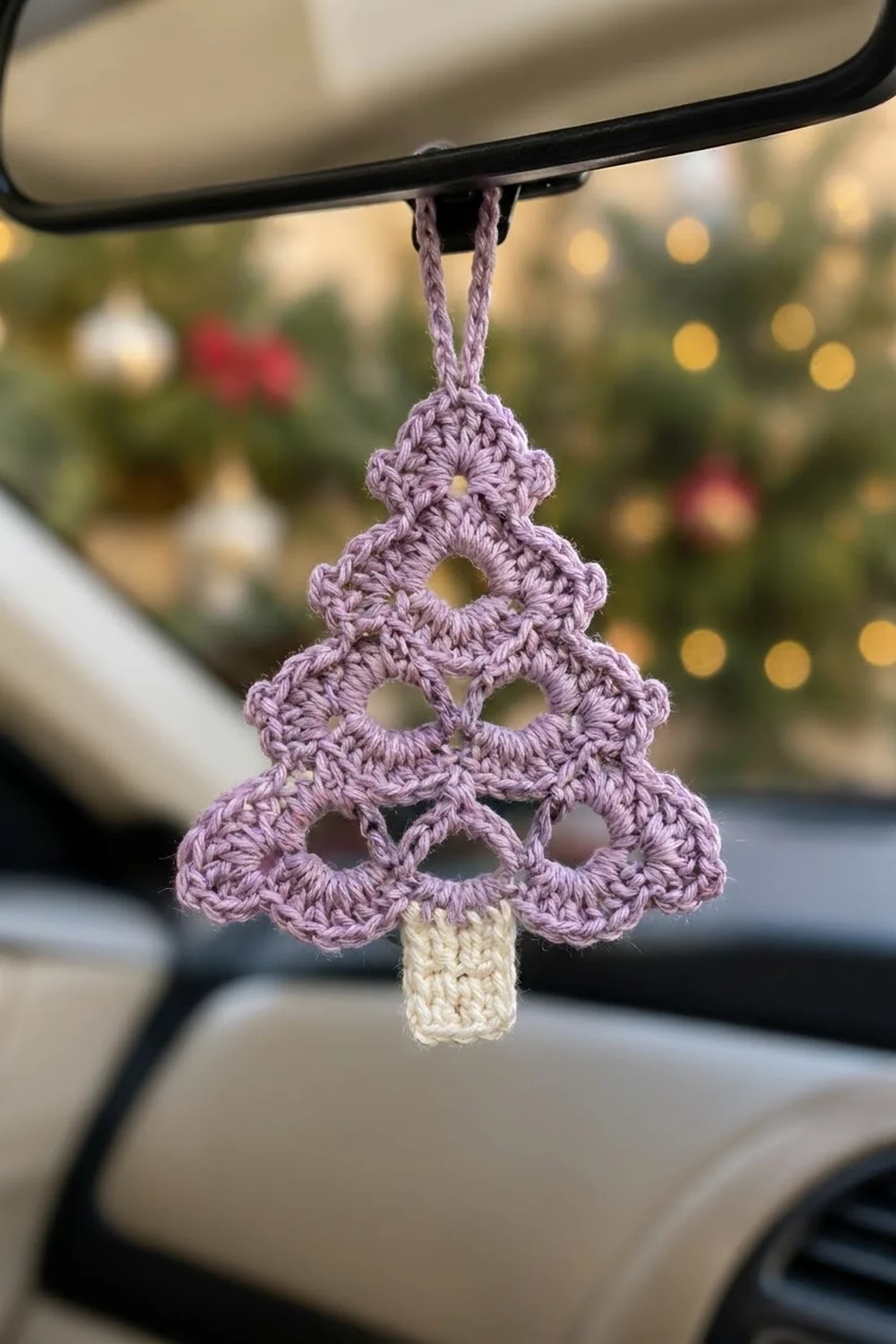 Lavender crochet Christmas tree ornament with lacy openings hanging from a car's rearview mirror.