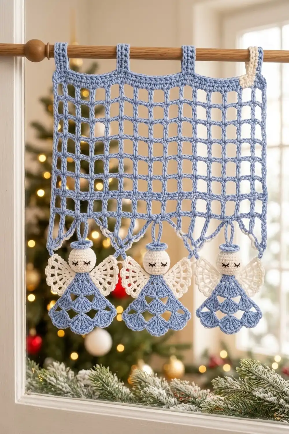 Crocheted blue and white angel ornaments hang from a lacy blue panel on a window with Christmas decorations.