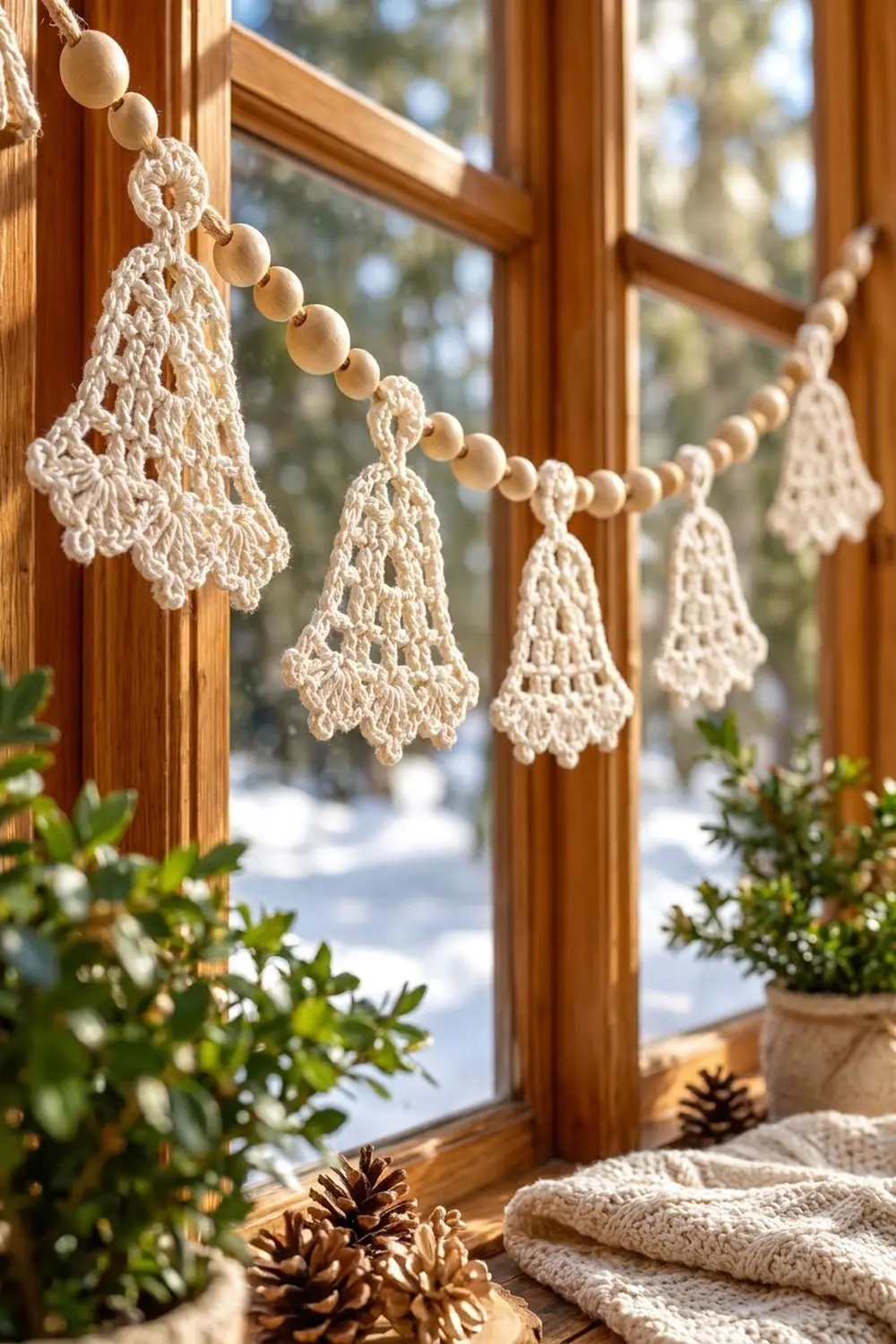 Crocheted lace bell garland with wooden beads draped across wooden window frame with winter view.