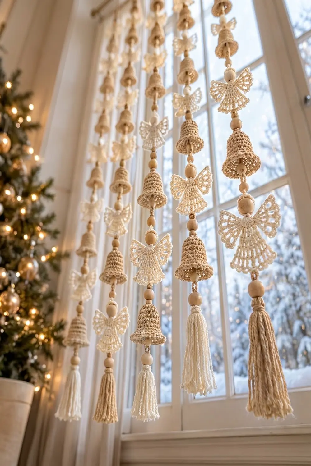 Beige crocheted bell and angel ornaments with tassels hang from window in festive holiday decoration.
