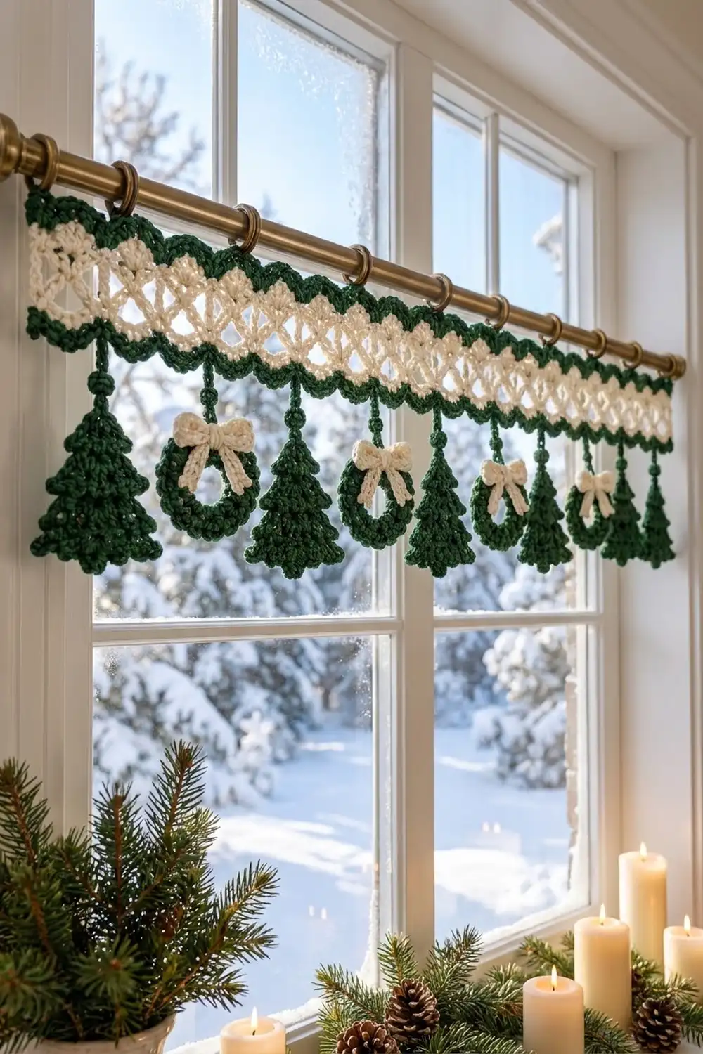 A crocheted green and cream garland with hanging trees and bows displayed on a brass rod above a snowy window.