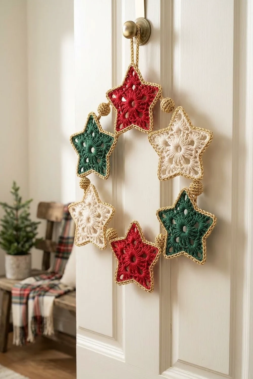 A crocheted star wreath in red, green, and cream hangs from a brass doorknob on a white paneled door.
