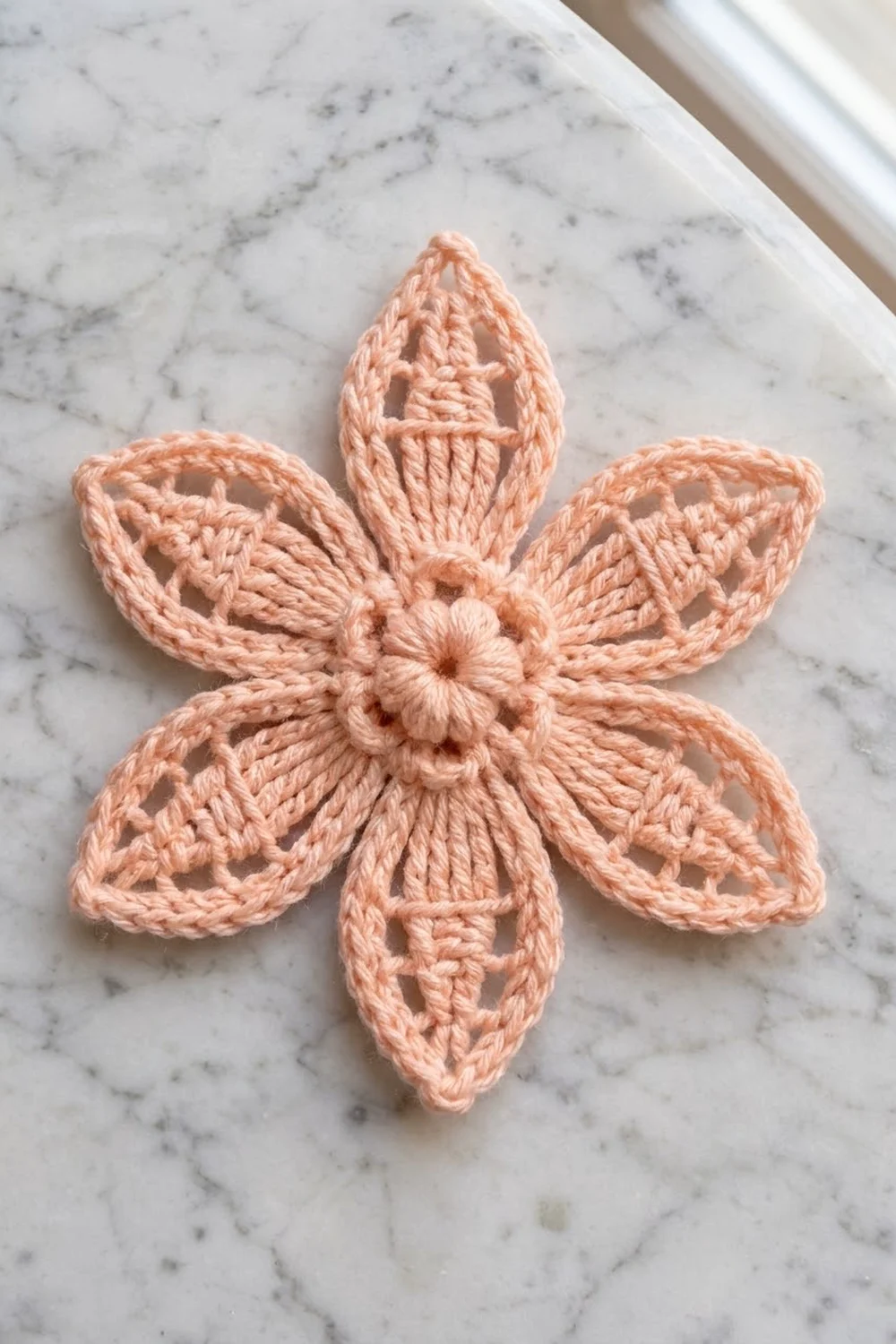 A delicate peach-colored crocheted flower with six petals displayed on white marble surface.