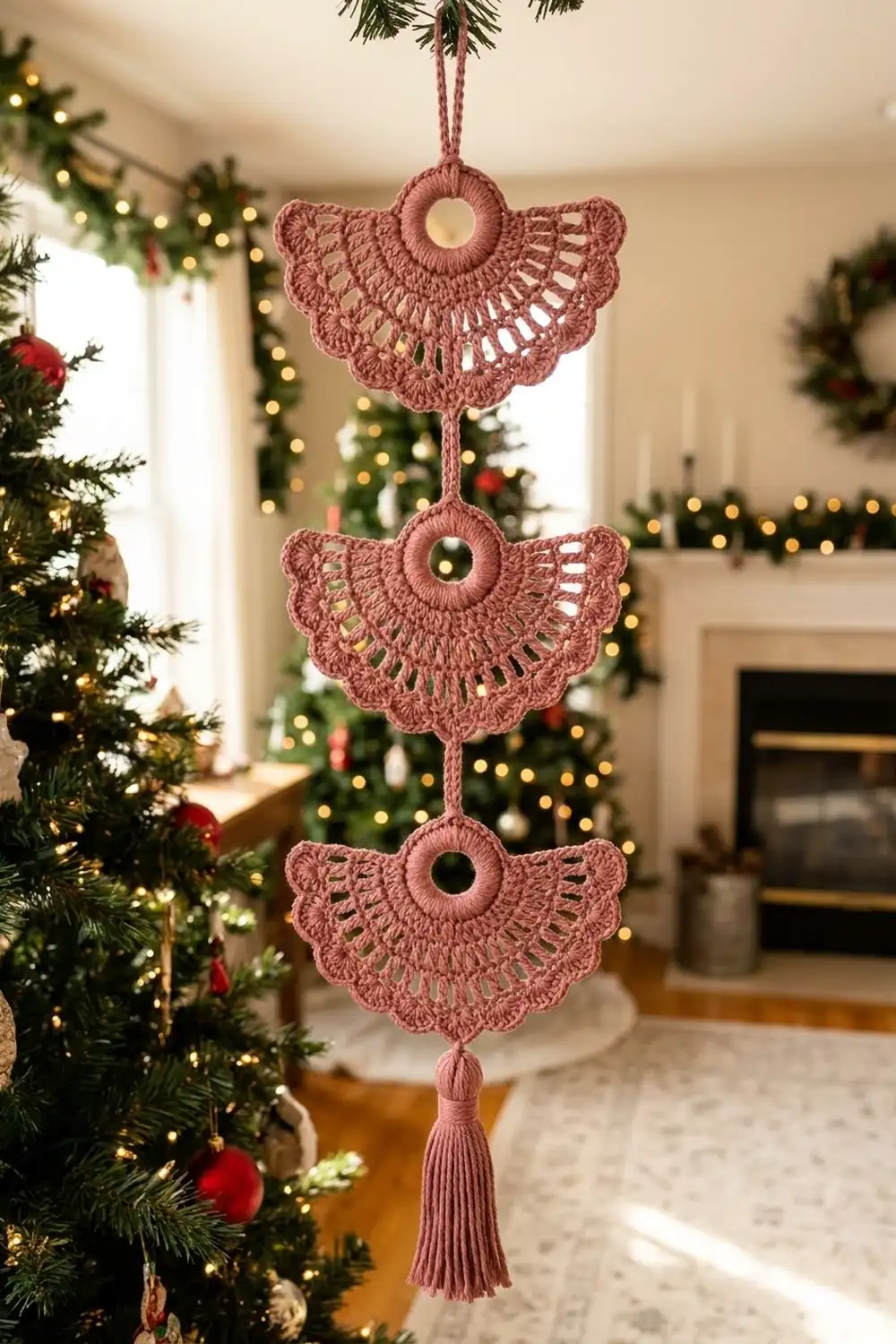 A dusty rose crocheted angel ornament hangs in a festive living room decorated with garland and Christmas lights.