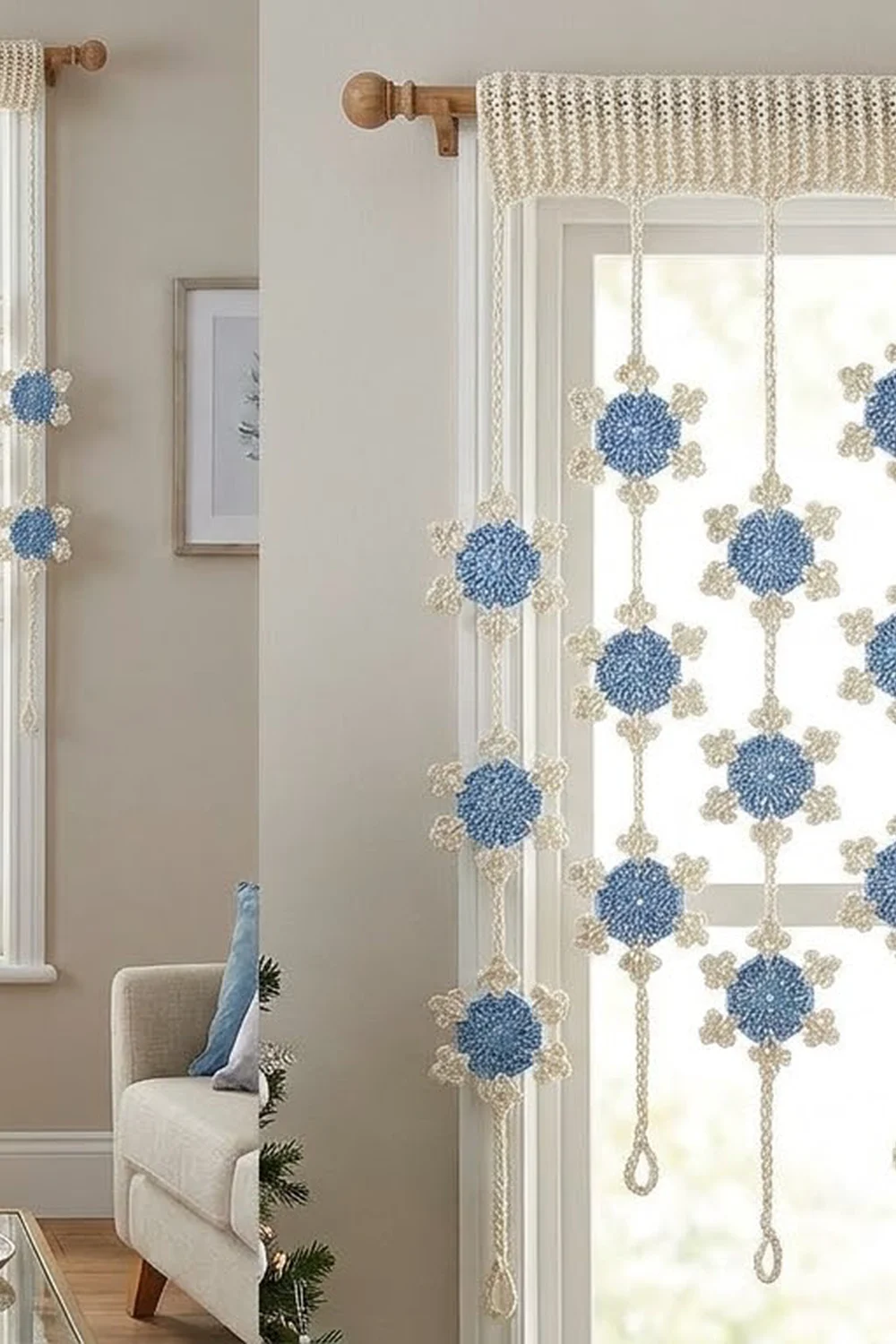 A cream linen curtain with blue and beige embroidered snowflake ornaments hangs from a wooden rod in a bright room.
