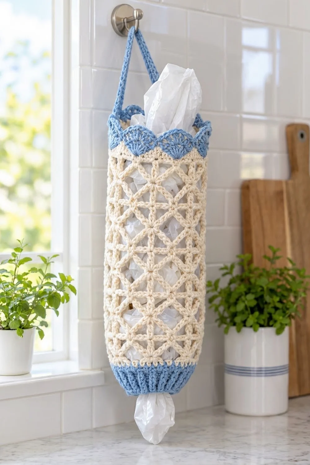 A crocheted tissue holder in cream and blue hangs on a bathroom wall filled with white tissues.