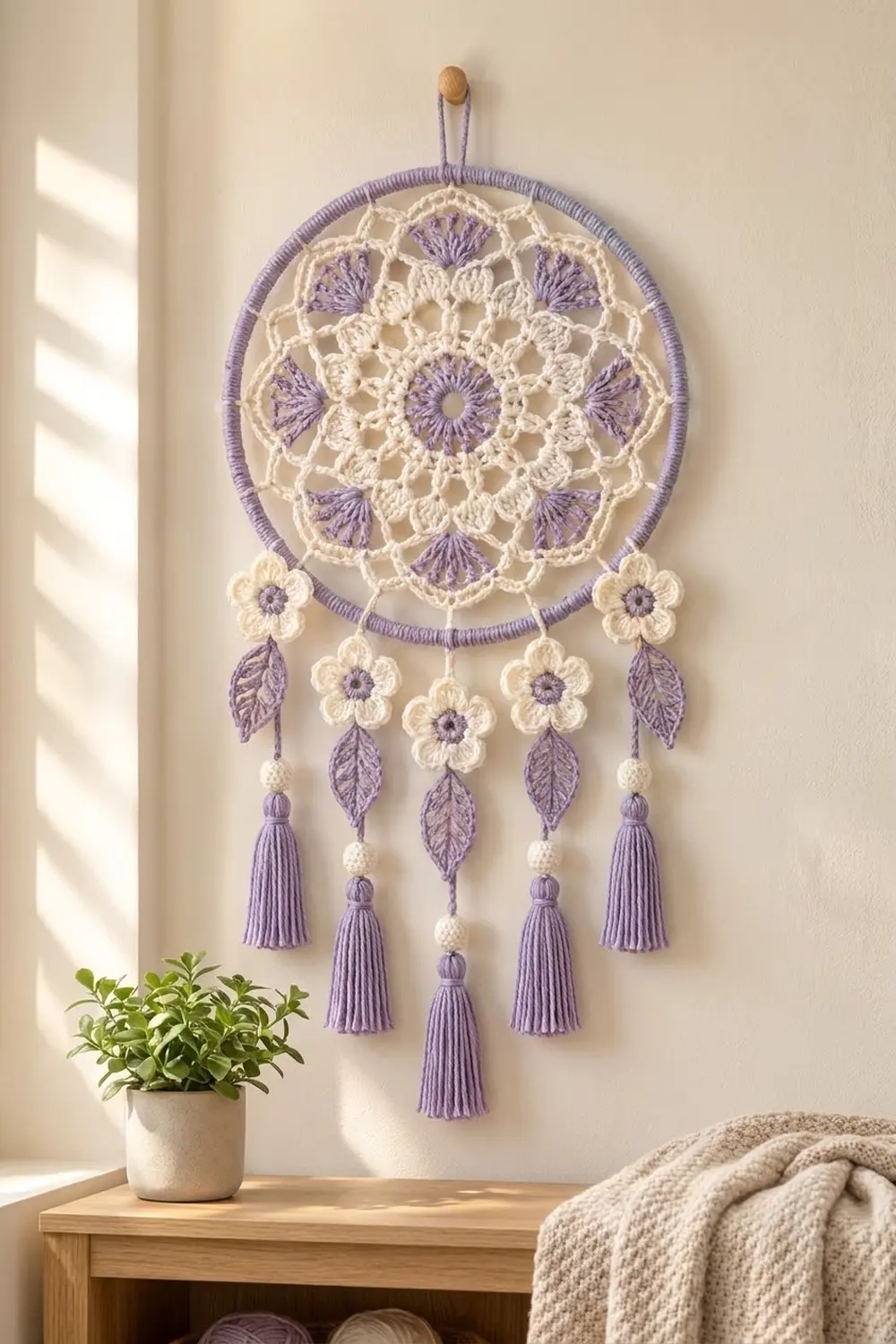 A purple and cream crocheted dreamcatcher hangs on a beige wall above a wooden shelf with a potted plant.