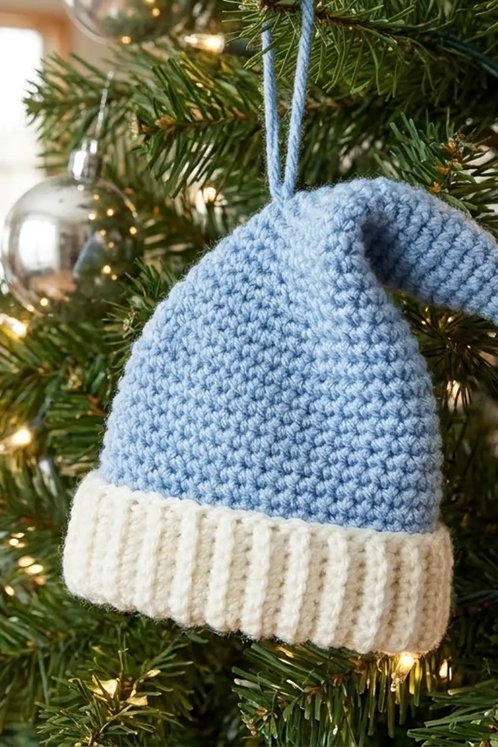 A blue and cream knitted pear ornament with a hanging loop displayed on a decorated Christmas tree branch.